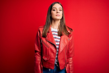 Young beautiful brunette woman wearing casual jacket standing over red background Relaxed with serious expression on face. Simple and natural looking at the camera.