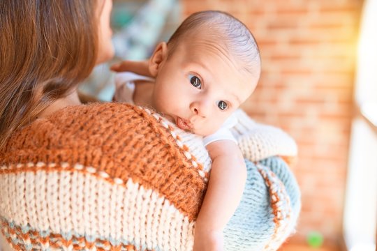 Young beautiful woman and her baby standing at home. Mother holding and hugging newborn
