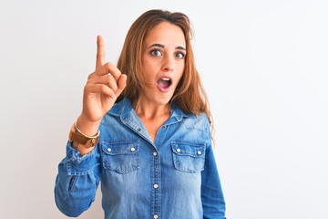 Young redhead woman wearing denim jacket standing over isolated background pointing finger up with successful idea. Exited and happy. Number one.