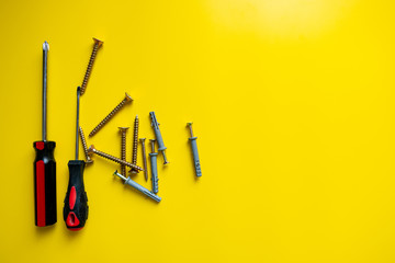 Many different nails screws nuts bolts screwdriver, utility knife on a bright yellow background of the copy space. Construction and repair concept