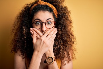 Beautiful brunette woman on vacation with curly hair and piercing wearing glasses and diadem shocked covering mouth with hands for mistake. Secret concept.