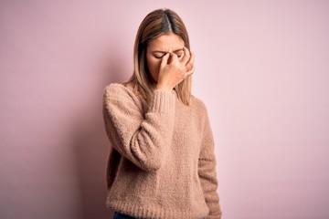 Young beautiful blonde woman wearing winter wool sweater over pink isolated background tired rubbing nose and eyes feeling fatigue and headache. Stress and frustration concept.