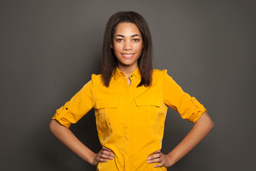 Black student girl in yellow shirt smiling on gray background