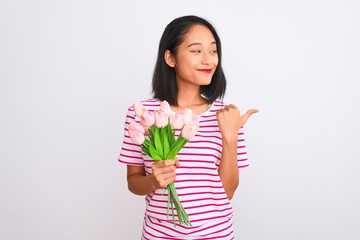 Young chinese woman holding bouquet of roses standing over isolated white background pointing and showing with thumb up to the side with happy face smiling