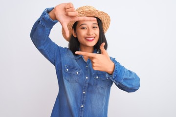 Young beautiful chinese woman wearing denim shirt and hat over isolated white background smiling making frame with hands and fingers with happy face. Creativity and photography concept.