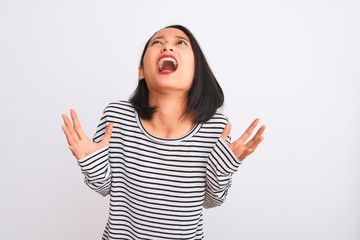 Young chinese woman wearing striped t-shirt standing over isolated white background crazy and mad shouting and yelling with aggressive expression and arms raised. Frustration concept.