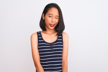 Young chinese woman wearing striped t-shirt standing over isolated white background winking looking...