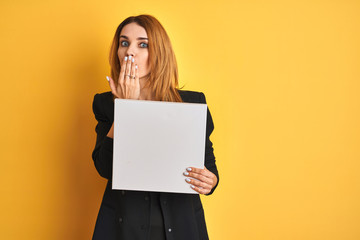 Young redhead businesswoman with clear eyes holding banner over isolated yellow background cover...
