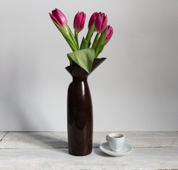 Pink tulips bouquet in brown vase and cup of coffee on white wooden background with copy space