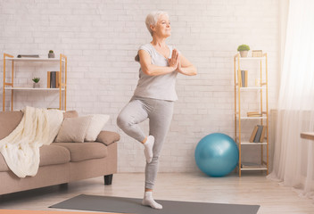 Senior woman doing yoga tree pose at home, free space