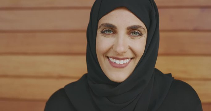 Portrait of confident muslim woman wearing a black hijab head scarf looking into the camera with a smile