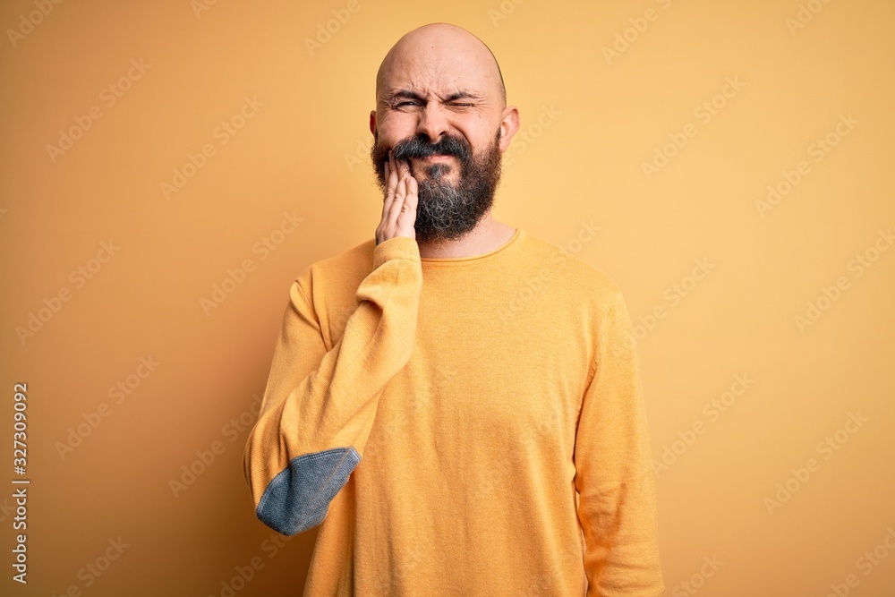 Poster handsome bald man with beard wearing casual sweater standing over yellow background touching mouth w