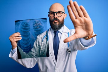Handsome bald doctor man with beard wearing stethoscope holding chest xray with open hand doing...