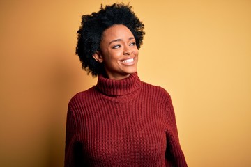 Fototapeta na wymiar Young beautiful African American afro woman with curly hair wearing casual turtleneck sweater looking away to side with smile on face, natural expression. Laughing confident.