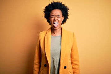 Fototapeta na wymiar Young beautiful African American afro businesswoman with curly hair wearing yellow jacket sticking tongue out happy with funny expression. Emotion concept.