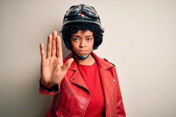 Young African American afro motorcyclist woman with curly hair wearing motorcycle helmet doing stop sing with palm of the hand. Warning expression with negative and serious gesture on the face.