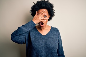 Fototapeta na wymiar Young beautiful African American afro woman with curly hair wearing casual sweater peeking in shock covering face and eyes with hand, looking through fingers with embarrassed expression.