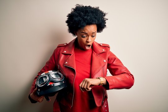 Young African American afro motorcyclist woman with curly hair holding motorcycle helmet Looking at the watch time worried, afraid of getting late