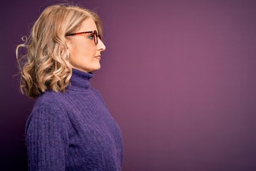 Middle age beautiful blonde woman wearing casual purple turtleneck sweater and glasses looking to...