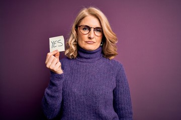 Middle age beautiful blonde woman wearing glasses holding reminder paper with yes message with a...
