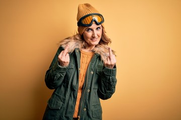 Middle age beautiful blonde skier woman wearing snow sportwear and ski goggles Showing middle finger doing fuck you bad expression, provocation and rude attitude. Screaming excited