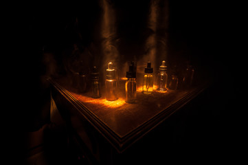 Smoke clouds and vape liquid bottles on dark background. Light effects. Useful as background or...