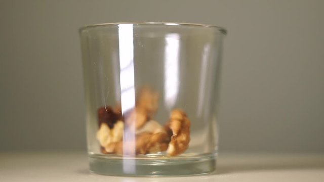 Fresh walnuts without shell in transparent glass with white reflection. Nuts pouring into an empty glass on a pastel background, close-up.