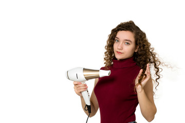 Beautiful joyful teenage girl drying long brown hair with a hair dryer over white background