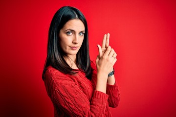 Young brunette woman with blue eyes wearing casual sweater over isolated red background Holding symbolic gun with hand gesture, playing killing shooting weapons, angry face