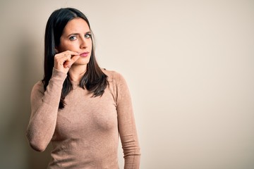 Young brunette woman with blue eyes wearing casual sweater over isolated white background mouth and lips shut as zip with fingers. Secret and silent, taboo talking