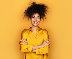 Obraz na płótnie Canvas Smiling girl holds hands crossed. Photo of african american girl on yellow background