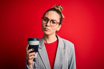 Young beautiful blonde businesswoman with blue eyes wearing glasses drinking cup of coffe with a confident expression on smart face thinking serious