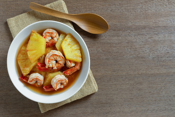 hot and sour pineapple soup with shrimp in a ceramic bowl on wooden table, top view. asian homemade style food concept.