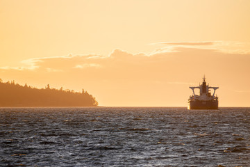 sunset on beach with rocks in the front and large  cargo boat near island  on water pacific ocean Pacific north west PNW Vancouver Canada boats waiting vertical photo 