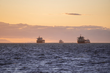 LARGE CARGO SHIPS AWAITING WAITING to get loaded on a coast during sunset golden hour in between mountains with scenic view at pacific ocean Pacific north west Vancouver Canada British Columbia 