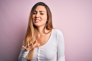 Fototapeta premium Young beautiful blonde woman with blue eyes wearing white t-shirt over pink background disgusted expression, displeased and fearful doing disgust face because aversion reaction.