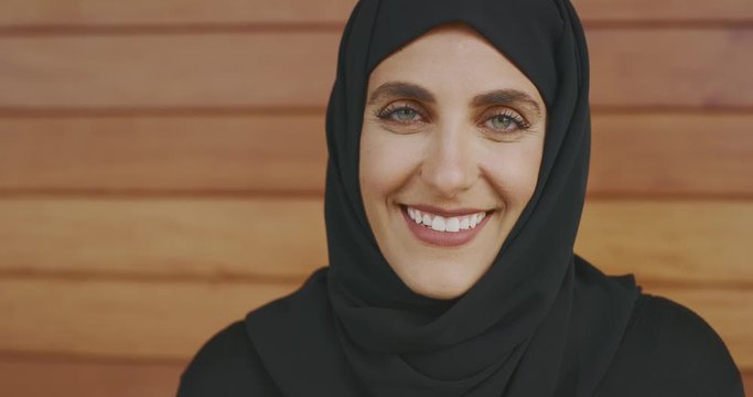 Portrait of a beautiful content muslim woman wearing a black hijab headscarf looking up into the camera with a smile and green eyes