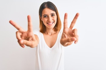 Beautiful redhead woman wearing casual white t-shirt over isolated background smiling looking to the camera showing fingers doing victory sign. Number two.