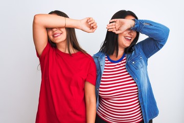 Young beautiful women wearing casual clothes standing over isolated white background covering eyes with arm smiling cheerful and funny. Blind concept.