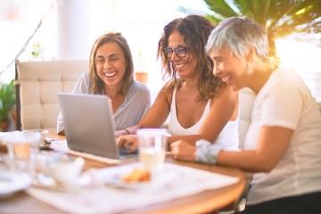 Meeting of middle age women having lunch and drinking coffee. Mature friends smiling happy using laptop at home on a sunny day