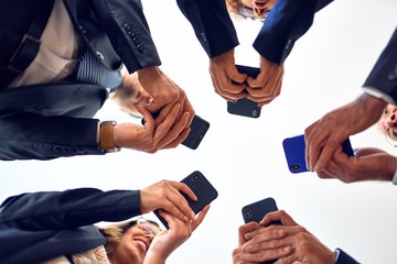 Group of business workers smiling happy and confident. Standing on a circle with smile on face using smartphone together at the office.