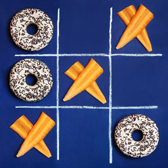 Conceptual photo: the battle between healthy food and junk food. Donuts and carrot slices in the...