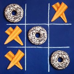 Conceptual photo: the battle between healthy food and junk food. Donuts and carrot slices in the...