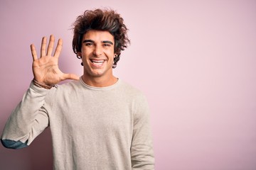 Young handsome man wearing casual t-shirt standing over isolated pink background showing and pointing up with fingers number five while smiling confident and happy.