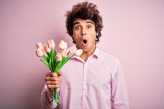 Young handsome man holding flowers standing over isolated pink background scared in shock with a surprise face, afraid and excited with fear expression