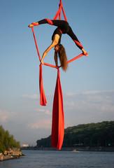 Beautiful and flexible female circus artist dancing with aerial silk with sky and river coastline...