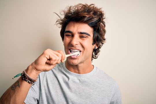 Young handsome man smiling happy. Standing with smile on face whasing tooth using toothbrush over isolated white background