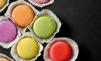 Colorful macarons cakes in paper baskets on black background. Top view. Copy space