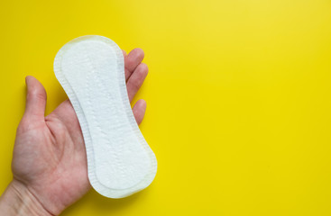 Woman's hand holding a daily sanitary pad on a bright yellow background close-up of copy space