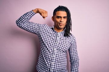 Young handsome african american afro man with dreadlocks wearing casual shirt Strong person showing arm muscle, confident and proud of power